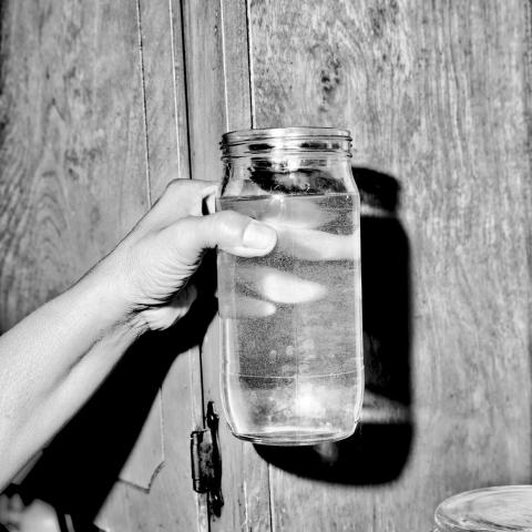 A black and white image of a hand holding a mason jar filled with water and floating particles