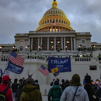 Insurrectionists stand in front of the capitol building holding American flags and Trump 2020 flags